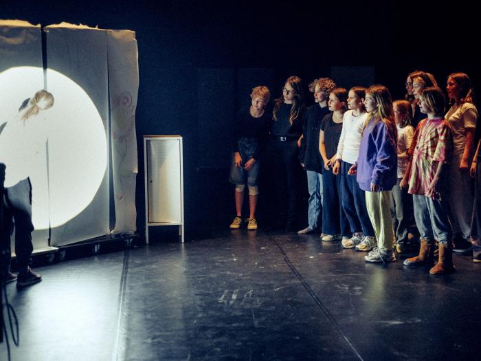 En gruppe børn kigger nysgerrigt mens et andet barn tegner på et stort stykke papir