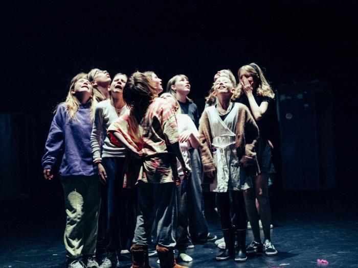 En gruppe af børn står tæt sammen på scenen og græder mod himlen