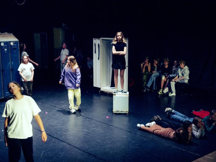 Mørk scene og skuespillere fordelt mellem skabe, nogle ligger, står på et skab, løber