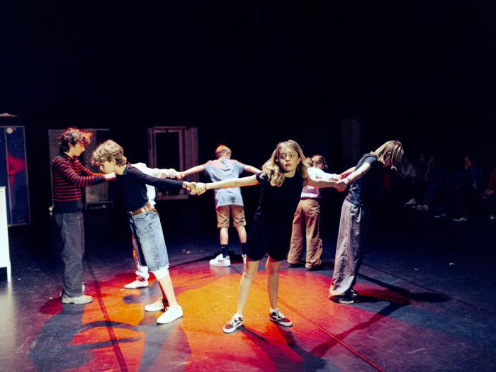 Børnene står i en rundkreds med ryggen til hinanden og holder hinanden i hænderne, mens de læner sig fremad 